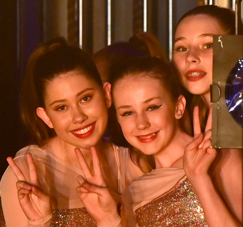 Three dancers backstage smiling and posing for the camera