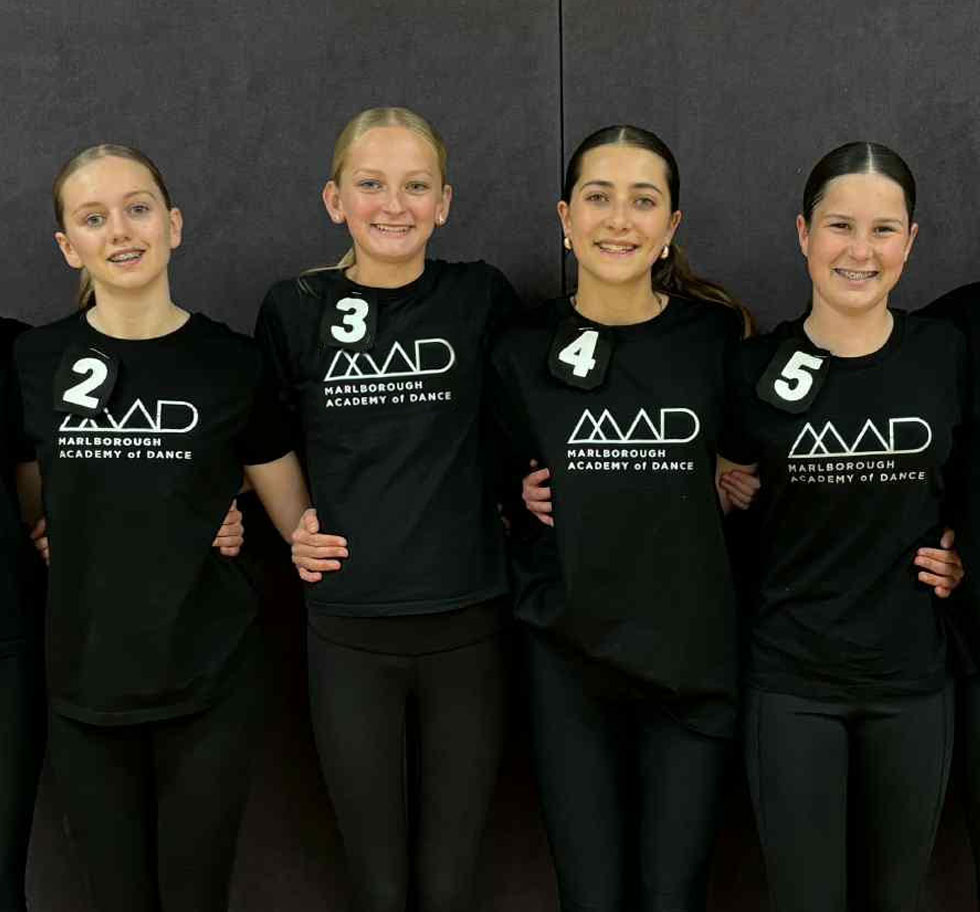 Four dancers lined up in the MAD uniform. The uniform is black with the MAD logo on the front